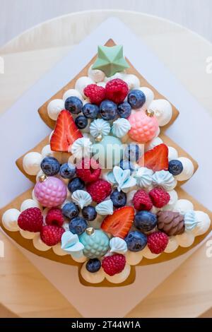 La torta a strati a forma di albero di natale è decorata con frutti di bosco freschi, cioccolato e fiori. La torta con crema di formaggio e torte al miele Foto Stock