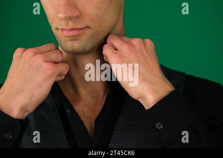 Primo piano delle mani di un uomo che raddrizza una camicia nera, regala un giubbotto classico, spalle da lati diversi, imposta tre foto su sfondo verde primo piano cromakey, capelli scuri Foto Stock