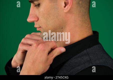 Primo piano delle mani di un uomo che raddrizza una camicia nera, regala un giubbotto classico, spalle da lati diversi, imposta tre foto su sfondo verde primo piano cromakey, capelli scuri Foto Stock