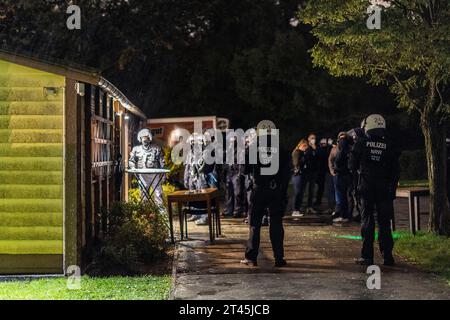 Gelsenkirchen, Germania. 28 ottobre 2023. Gli agenti di polizia si trovano di fronte alla clubhouse di un giardino di assegnazione, mentre i partecipanti a un concerto di destra sono guidati uno ad uno e presi per l'identificazione. La polizia ha posto fine a un evento di sospetti sostenitori della scena di destra a Gelsenkirchen. Secondo i primi risultati della polizia, circa 80 persone si erano riunite per un concerto in un circolo di un giardino di assegnazione il sabato sera. Credito: Christoph Reichwein/dpa/Alamy Live News Foto Stock