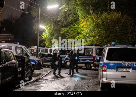 Gelsenkirchen, Germania. 28 ottobre 2023. I veicoli della polizia sono parcheggiati sulla strada di fronte all'ingresso del giardino d'assegnazione, mentre gli agenti di polizia proteggono una scena. La polizia ha posto fine a un evento di sospetti sostenitori della scena di destra a Gelsenkirchen. Secondo i primi risultati della polizia, circa 80 persone si erano riunite per un concerto in un circolo di un giardino di assegnazione il sabato sera. Credito: Christoph Reichwein/dpa/Alamy Live News Foto Stock