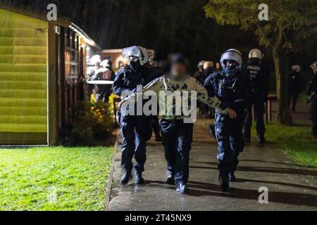 Gelsenkirchen, Germania. 28 ottobre 2023. Gli agenti di polizia si trovano di fronte alla clubhouse di un giardino d'assegnazione, mentre i partecipanti a un sospetto concerto di destra sono guidati uno ad uno e presi per l'identificazione. La polizia ha posto fine a un evento di sospetti sostenitori della scena di destra a Gelsenkirchen. Secondo i primi risultati della polizia, circa 80 persone si erano riunite per un concerto in un circolo di un giardino di assegnazione il sabato sera. Credito: Christoph Reichwein/dpa/Alamy Live News Foto Stock
