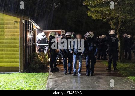 Gelsenkirchen, Germania. 28 ottobre 2023. Gli agenti di polizia si trovano di fronte alla clubhouse di un giardino di assegnazione, mentre i partecipanti a un concerto di destra sono guidati uno ad uno e presi per l'identificazione. La polizia ha posto fine a un evento di sospetti sostenitori della scena di destra a Gelsenkirchen. Secondo i primi risultati della polizia, circa 80 persone si erano riunite per un concerto in un circolo di un giardino di assegnazione il sabato sera. Credito: Christoph Reichwein/dpa/Alamy Live News Foto Stock