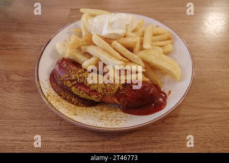 Vista dall'alto, currywurst, salsiccia di maiale grigliata con curry in polvere servito con salsa ketchup al curry e patate fritte su piatto bianco e tavolo in legno Foto Stock