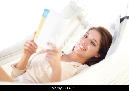 Donna felice, relax e lettura di libri su amaca per vacanze, weekend o vacanze a casa. Persona femminile, sdraiata e sorridente con romanzo in conforto Foto Stock