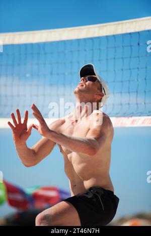 Pallavolo, esercizio fisico e uomo in spiaggia in gara, partita o partita estiva all'aperto. Sport, fitness e atleta a terra per allenamenti, allenamenti e. Foto Stock