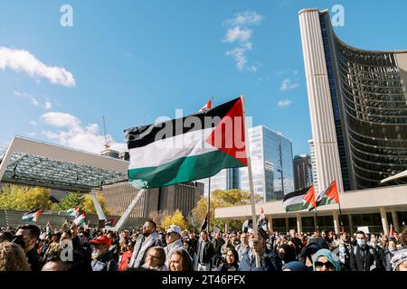 Toronto, Canada - 28 ottobre 2023: I manifestanti si riuniscono in una piazza della città, sventolando bandiere palestinesi tra moderni grattacieli sotto un cielo azzurro Foto Stock