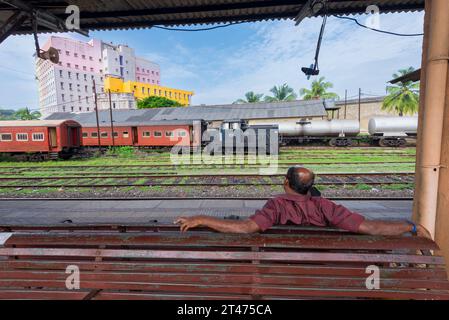 Un uomo siede su una panchina in attesa di un treno alla stazione ferroviaria di Galle nel sud dello Sri Lanka Foto Stock