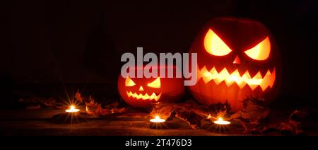 Tre lanterne in zucca di Halloween e candele accese su sfondo di legno scuro Foto Stock