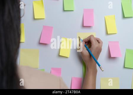 Donna creativa che scrive su appunti adesivi vuoti sul muro Foto Stock
