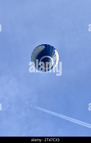 Mongolfiera blu in un cielo azzurro visto dal basso, mentre un aereo che passa lascia dietro i contrafforti Foto Stock