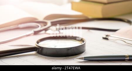 stetoscopio, lente di ingrandimento, penna e libri poggiati sugli elettrocardiogrammi sul tavolo Foto Stock