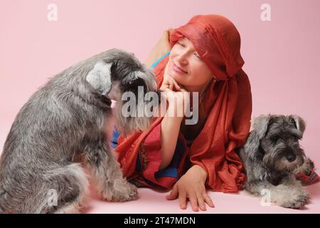 Donna matura con due cani schnauzer in miniatura su sfondo rosa Foto Stock