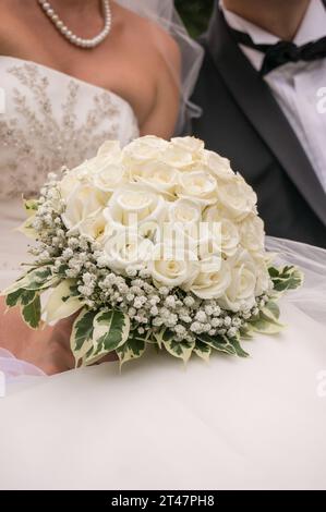 Un bouquet di nozze con rose nelle mani della sposa e dello sposo accanto a lei Foto Stock