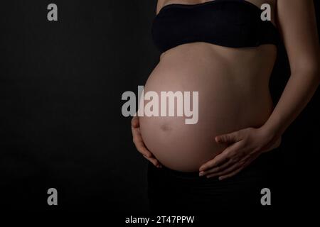 Primo piano la pancia di una donna incinta su sfondo nero con spazio per le copie Foto Stock