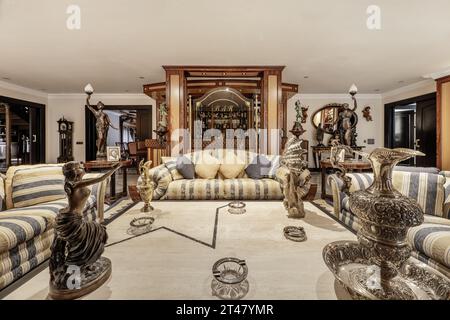 Grande soggiorno in una casa di lusso con decorazioni ornate con molte figure decorative, pavimenti in marmo bianco con bordo nero, tappeti, mobili in legno Foto Stock