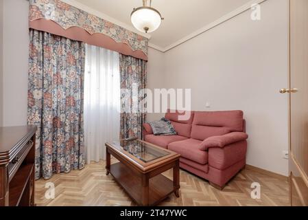 Soggiorno di una casa con una poltrona in tessuto rosso, tavolo interno in legno verniciato e vetro Foto Stock