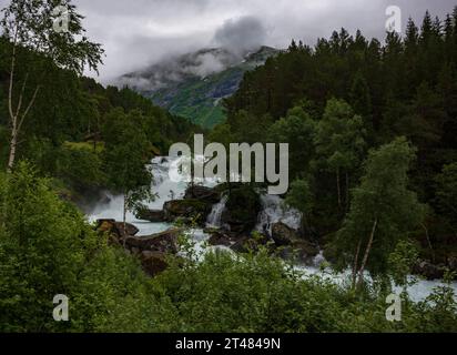 Le rapide di un torrente di montagna scorrono lungo la strada panoramica norvegese Gaularfjellet tra Moskog e Balestrand durante una giornata turbolenta. Foto Stock