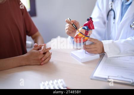 Le donne del medico cardiologo asiatico spiegano circa anatomico del modello di cuore umano al paziente femminile dopo aver esaminato la salute mentre dà consulenza abou Foto Stock