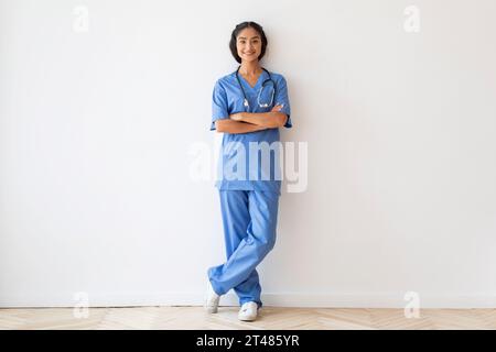 Sorridente giovane medico indiano donna in posa con le braccia piegate Foto Stock