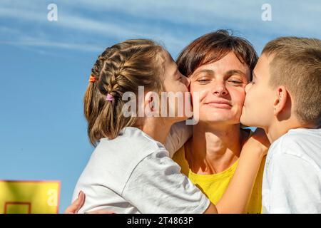 Abbracci all'aperto: La madre e i bambini adolescenti si coccolano delicatamente al sole sul campo da basket Foto Stock
