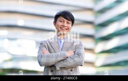 Allegro giovane uomo d'affari giapponese in piedi con le braccia piegate all'esterno Foto Stock
