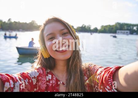 giovane latina che prende un selfie con barche sullo sfondo. sorridente donna turistica con denti bianchi e capelli lunghi. Foto Stock