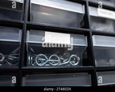 Vano portaoggetti in un'officina con etichetta bianca vuota sul contenitore. I ganci a vite si trovano nel vano e non sono in plastica. Fai da te l'hardware. Foto Stock