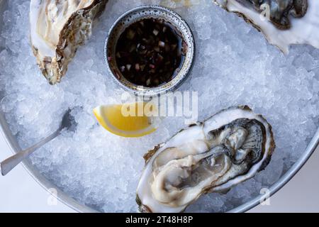 Le ostriche fresche a metà del guscio vengono servite in un piatto con ghiaccio, limoni e salsa. Il concetto di nutrizione sana. Foto Stock