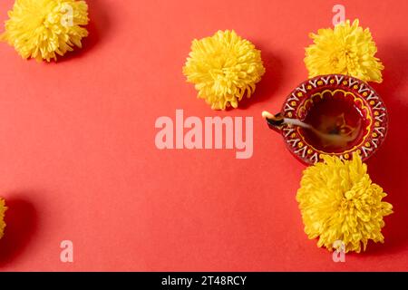 Biglietto d'auguri per il festival Happy Diwali e Kartika Deepam - colorata argilla Deepam con fiori gialli su sfondo rosso Foto Stock