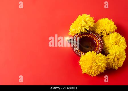 Biglietto d'auguri per il festival Happy Diwali e Kartika Deepam - Deepam in argilla colorata con fiori gialli su sfondo rosso Foto Stock