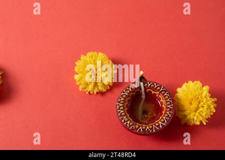 Auguri per il festival Happy Diwali e Kartika Deepam - colorata argilla Deepam con fiori gialli su sfondo rosso Foto Stock