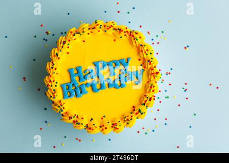 Torta di compleanno gialla con auguri di buon compleanno blu e cosparge di zucchero su sfondo blu Foto Stock