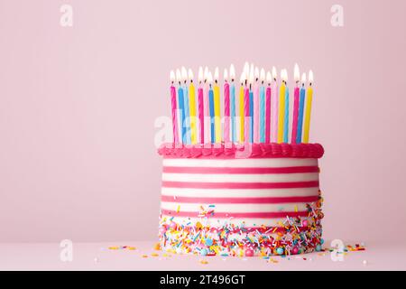 Torta di compleanno decorata con crema di burro a righe rosa e bianche e tante candele di compleanno su sfondo rosa Foto Stock