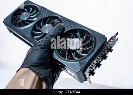 la mano di un tecnico informatico contiene una potente e moderna scheda per videogiochi per un computer con tre fan. Il concetto di hardware per PC. Video car di gioco Foto Stock