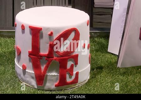 Una bella torta bianca con la parola AMORE scritta in rosso circondata da erba verde e uno sfondo semplice. Un'immagine perfetta per celebrare amore e dolcezza Foto Stock