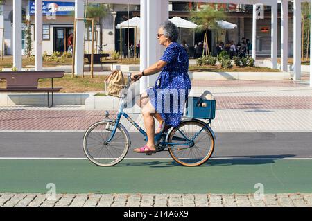 Una donna anziana cavalca con grazia una bicicletta classica con un affascinante cestino frontale Foto Stock