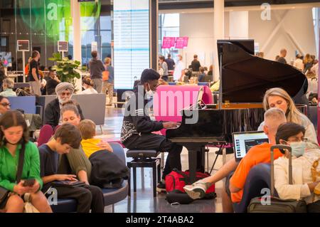 Montreal, Quebec, Canada - 07 04 2022: Un musicista adolescente che indossa una felpa nera Unbreakable con cappuccio che suona il pianoforte a coda nero in mezzo a un affollato e affollato outbound Foto Stock