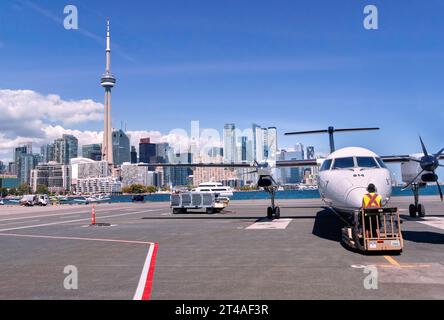 Moderno aereo di linea a turboelica bianco con eliche nere a sei pale seduto sull'asfalto dell'Aeroporto di Toronto City separato da un tratto di acque blu Foto Stock