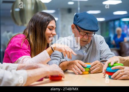 Infermiera che consigliava un uomo anziano che giocava a giochi di abilità in una casa di cura Foto Stock