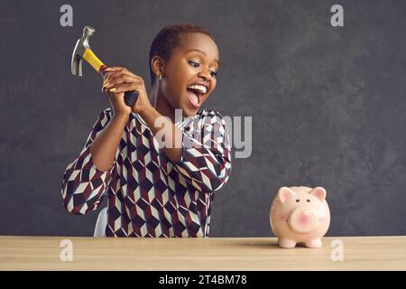 Una donna afro-americana emotivamente agitata che ha bisogno di soldi vuole rompere la scatola dei soldi. Foto Stock