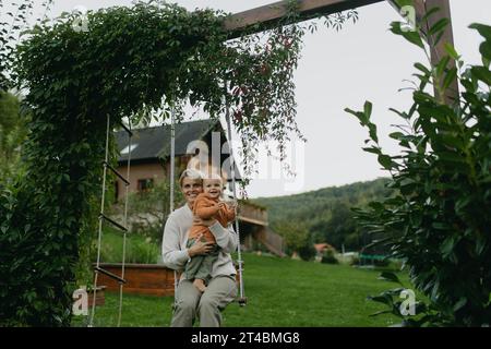 La bella madre e il bambino si muovono in giardino, divertendosi e trascorrendo momenti di qualità all'aperto durante le calde giornate autunnali. Foto Stock