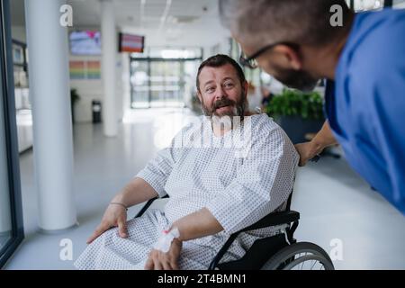 Infermiera di supporto che lenisce un paziente preoccupato in sedia a rotelle. Malattie e malattie nella salute degli uomini di mezza età. Medico compassionevole che parla con Foto Stock