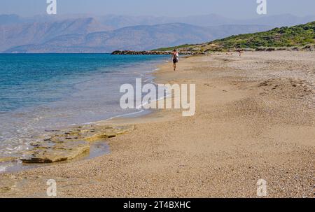 Uomo che cammina lungo la spiaggia di Almiros verso Capo Agia Ekatarinis sulla costa nord di Corfù con le lontane montagne dell'Albania - Isole Ionie Grecia Foto Stock