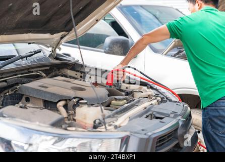 Tecnico che carica la batteria dell'auto con cavi ponte per corrente elettrica in officina. Foto Stock