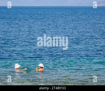 Due signore che indossano cappelli bianchi che chiacchierano in mare a Corfù, nelle Isole Ionie della Grecia Foto Stock