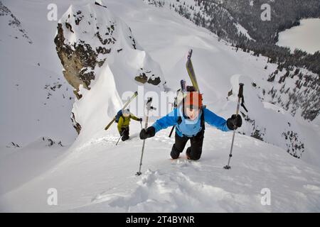 Donna che cammina su una pista da neve con gli sci in valigia, British Columbia, Canada Foto Stock