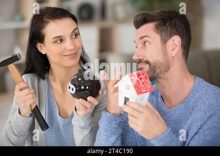 giovane coppia rompendo la banca piggy con il martello a casa Foto Stock