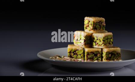 Un piatto di dolci arabi con pistacchi raffigurati su uno sfondo bianco e uno sfondo grigio e nero Foto Stock