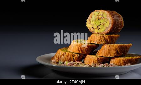 Un piatto di dolci arabi con pistacchi raffigurati su uno sfondo bianco e uno sfondo grigio e nero Foto Stock